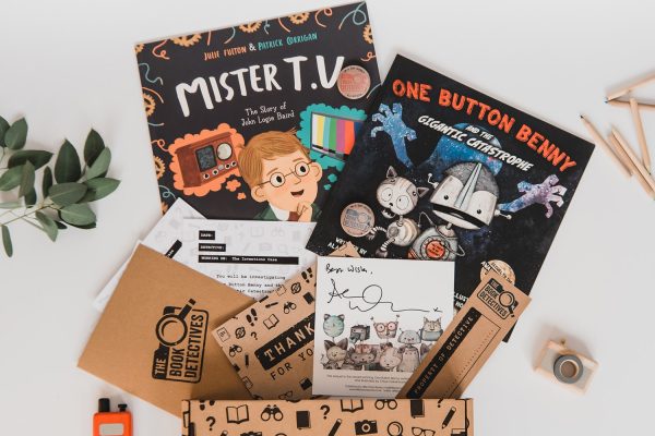 The image shows the contents of a book box. There are two books, activity sheets, two badges and a bookmark laid out on a white background.